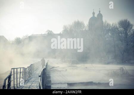 silhouette d'un homme qui traverse le pont au-dessus de la rivière avec des condensats hiver givré matin Banque D'Images