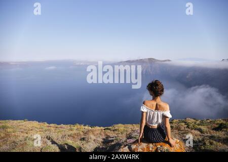 Une jeune femme est assise au bord d'une montagne et bénéficie de la vue Banque D'Images