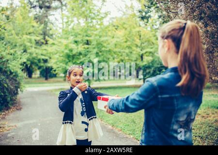 Bonne petite fille donnant une boîte cadeau à son ami excité. Les gens, les enfants, les vacances, les amis et le concept d'amitié Banque D'Images