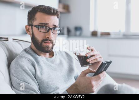 Close up. Un jeune homme avec un smartphone assis dans une chaise confortable Banque D'Images