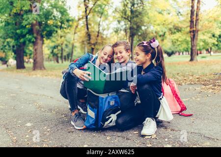 Retour à l'école. Les enfants avec des sacs à dos ont du plaisir, de parler, de lire un livre.Groupe d'écoliers élémentaires ayant une discussion sur les devoirs pendant que goi Banque D'Images