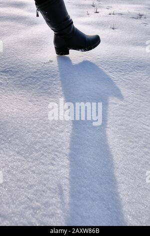 La chaussure haute féminine jette une longue ombre sur la neige à la lumière du soleil couchant; la première étape, le début du chemin, entre dans la zone de unkn Banque D'Images