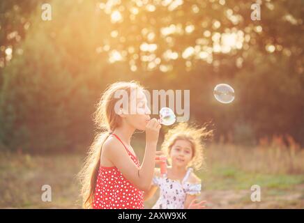 Deux Petites filles Mignonnes soufflant des bulles de savon en plein air le jour d'été - bonne enfance Banque D'Images