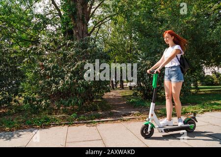 Une femme conduit sur un scooter électrique le long de la rue ensoleillée Banque D'Images