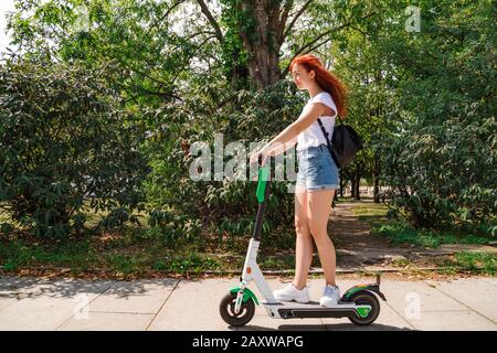 Une femme conduit sur un scooter électrique le long de la rue ensoleillée Banque D'Images