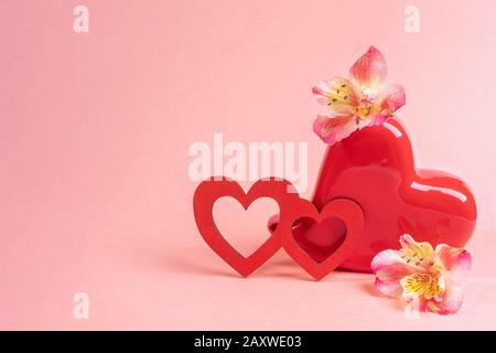 Vase rouge en forme de coeur avec fleurs alstroemeria et deux coeurs en bois rouge sur rose. Saint Valentin fond festif. Espace de copie pour le texte. Banque D'Images