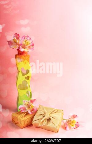 Branché enveloppé dans un tissu doré dans des boîtes cadeaux de la technique Furoshiki, vase avec des coeurs peints à la main, fleurs Alstroemeria sur fond rose avec bo Banque D'Images