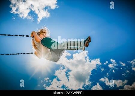 fille sur une balançoire atteignant les nuages sur un chaud après-midi d'été Banque D'Images