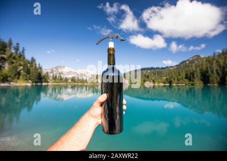 Homme tenant une bouteille de vin tout en profitant de la vue sur le lac. Banque D'Images