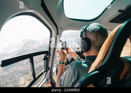 Un homme à la retraite prend des photos avec son téléphone depuis l'hélicoptère. Banque D'Images