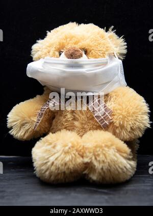 Ours en peluche dans un masque en tissu médical sur fond noir. Banque D'Images