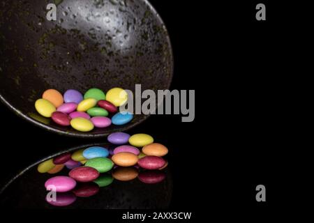 Beaucoup de bonbons doux colorés dans un bol glacé isolé sur le verre noir Banque D'Images
