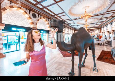 28 novembre 2019, Emirats Arabes Unis, Dubaï: Une jeune fille touristique frottant une drôle de sculpture de chameau dans le centre commercial de Dubaï Banque D'Images
