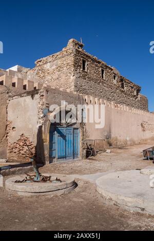 Rue avec un vieux bâtiment abandonné en pierre. Porte bleue correspondant au ciel bleu vif. La vieille ville - médina d'Essaouira, Maroc. Banque D'Images