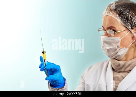 Un médecin dans un gant médical en latex vérifie le vaccin à partir d'une petite seringue. Le concept de protection contre les virus. Thème médical sur un turquoi léger Banque D'Images
