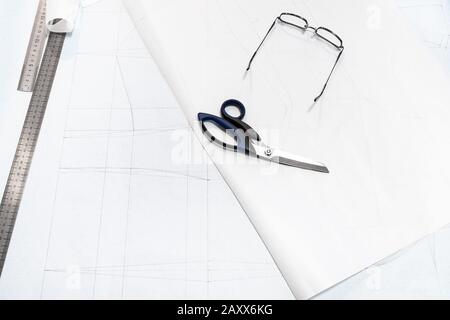 règle en acier, ciseaux de tailleur et lunettes se trouvent sur des feuilles de papier de traçage avec un motif de robe femelle sur la table Banque D'Images