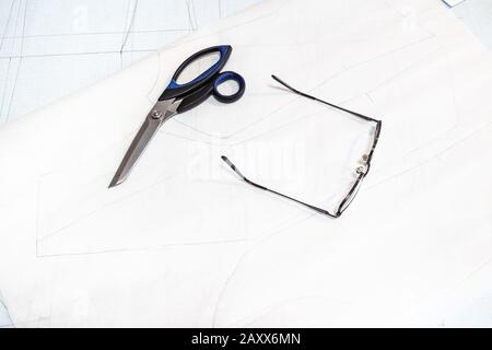 les ciseaux et les lunettes de tailleur se trouvent sur des feuilles de papier de traçage avec un motif de robe féminine sur la table Banque D'Images