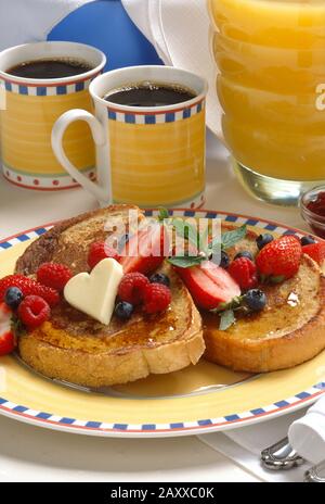 Un brunch ou un petit-déjeuner de pain grillé accompagné de fraises, de bleuets et de beurre en forme de coeur avec café et jus d'orange. Banque D'Images