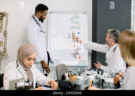 Professeur d'âge mûr enseignant à un groupe d'étudiants en médecine multiethnique de la classe moderne, ayant une discussion sur les nouvelles molécules chimiques, avec l'Afrique Banque D'Images