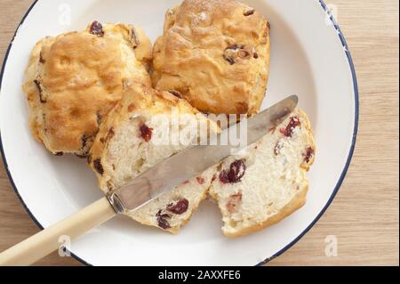 Scone de pain fraîchement cuit en tranches avec raisins secs fruités sur une plaque avec deux scones non coupés, vue au-dessus de la tête avec un couteau Banque D'Images