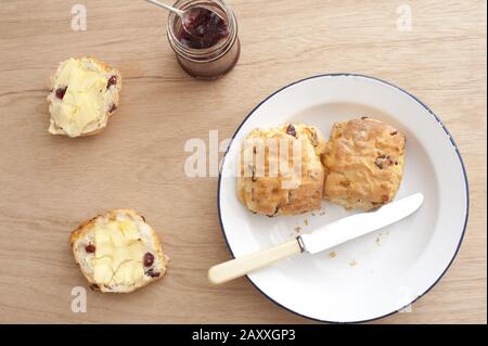 Des scones de fruits maison fraîchement cuits au beurre servis sur une plaque et une table en bois avec un bol de confiture de baies, vue sur le dessus Banque D'Images