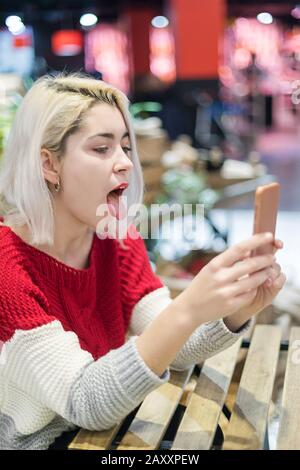 Beau modèle féminin dans les tons poses à la caméra de son téléphone portable, fait selfie pendant qu'il est assis à la cafétéria. Le jeune prend la photo d'elle-même Banque D'Images