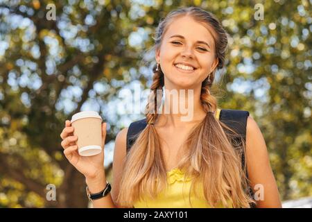 Belle jeune fille étudiant buvant le caffee sur le chemin de l'université ou de l'université. Mode habillée pour l'école portant ses livres et son carnet Banque D'Images