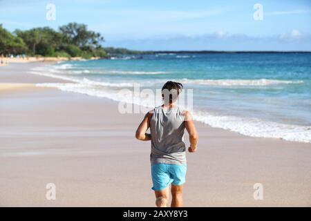 L'athlète de l'homme s'éloignant de derrière sur la plage au coucher du soleil. Coureur d'homme faisant de l'exercice cardio sur le sable avec fond de l'océan. Une vie active saine sur la destination de voyage. Banque D'Images