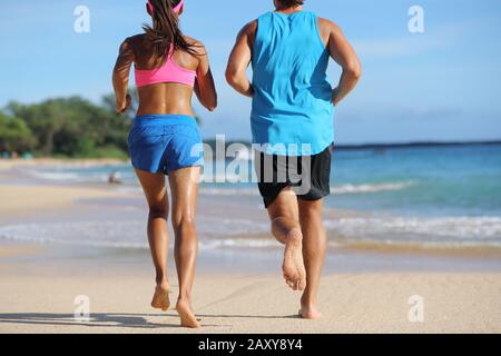 Deux athlètes coureurs couple courir ensemble sur la plage. Les gens de derrière le jogging loin pieds nus sur le sable sur la destination de voyage tropicale. Bas du corps, jambes, pieds. Banque D'Images