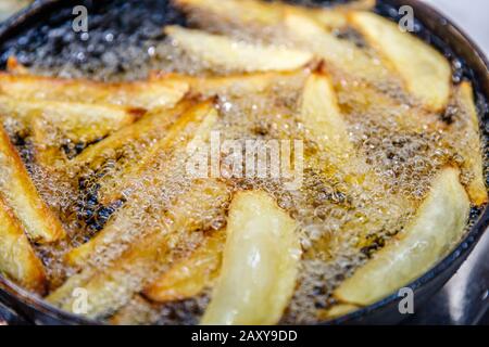 Les pommes de terre assaisonnées frire dans de l'huile chaude sur une poêle à frire en fonte. Processus. Banque D'Images