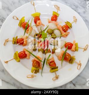 Brochettes de bambou avec oignon mariné, saumon salé, olives vertes, cornichons et tomates cerises. Apéritif à cocktail. Servi sur une plaque en céramique blanche. Banque D'Images