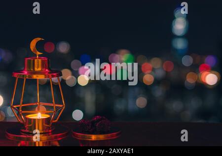 Lanterne dorée moderne avec symbole de lune sur le dessus et petite assiette de dattes fruits avec des lumières de ville colorées pour la fête musulmane du Saint lun Banque D'Images