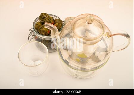 Fleurs de boules de thé dans un pot en verre, une théière en verre et un verre sur un fond blanc. Gros plan Banque D'Images