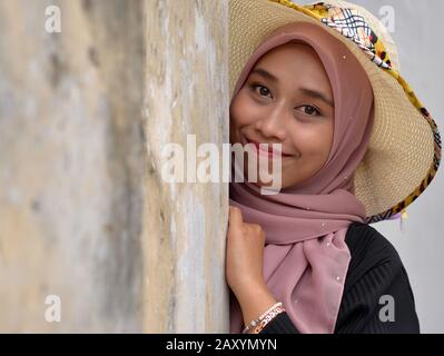 Belle jeune Malay malaisienne porte un chapeau de soleil moderne avec son hijab traditionnel et pose pour l'appareil photo. Banque D'Images