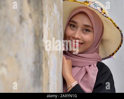 Belle jeune femme malaisienne porte un chapeau de soleil moderne avec son hijab traditionnel et sourires pour l'appareil photo. Banque D'Images