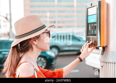 Une fille appuie sur un bouton pour traverser un passage pour piétons réglable sur une rue animée. Concept de développement urbain Banque D'Images