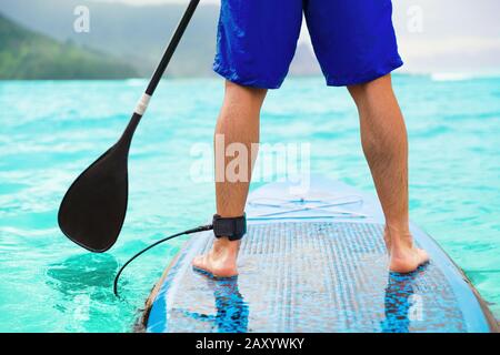 Paddle board homme faisant paddleboard debout sur l'océan. Paddleboard d'athlète sur le panneau de surf SUP lors d'un voyage à Hawaï sur la plage. Gros plan des jambes debout à bord. Banque D'Images