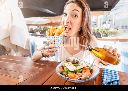 Une jeune fille touristique gaie essaie de déguster une cuisine grecque dans un restaurant local. Sur la table salade traditionnelle Horiatiki et Gyros à Pita Banque D'Images
