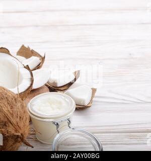 L'huile de noix de coco dans un bocal en verre hermétique et les plaques sur la table en bois blanc libre Banque D'Images