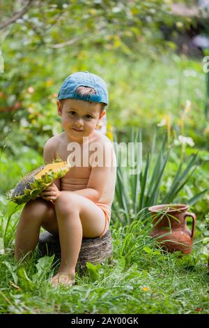 Petit garçon tenant une tête de tournesol mûre. Un joli petit garçon dans une casquette de baseball est assis sur une bosse. Enfants Mangeant Des Graines De Tournesol Banque D'Images