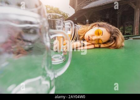 Jeune fille asiatique ivre avec gueule dormant à Biergarten avec des tasses à bière vides Banque D'Images