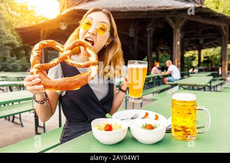 Une fille asiatique mangeant du Pretzel traditionnel et buvant de la bière bavaroise fraîche dans le jardin à bière de Munich. Le concept de festival alimentaire traditionnel et de tourisme Banque D'Images