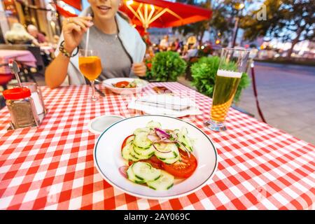 Une heureuse fille asiatique boit une tasse de bière lager dans un restaurant bavarois traditionnel et des en-cas sur une salade fraîche. Concept de cuisine gastronomique allemande Banque D'Images