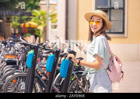 Femme asiatique louant un scooter électrique de coup de pied dans la rue de la ville. Concept moderne de partage des transports urbains Banque D'Images