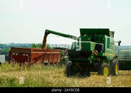 Transfert du grain d'une moissonneuse-batteuse John Deere T670 Hillmaster vers une remorque agricole lors de la récolte du blé près de Duras, Lot-et-Garonne, France. Banque D'Images