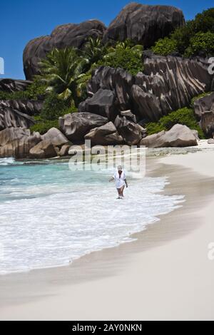 Une femme marche sur la plage de Grand Anse avec les champs typiques de granit de la Digue Banque D'Images