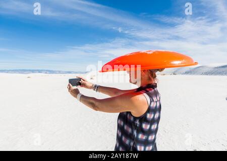 Femme portant un traîneau orange sur sa tête, prenant selfie, White Sands Nat'l Monument, NM Banque D'Images