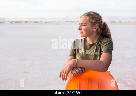Portrait d'une jeune fille de 13 ans se penchant sur un traîneau orange, White Sands Nat'l Monument, NM Banque D'Images