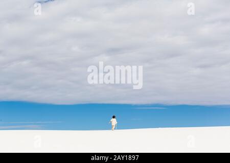 garçon de 6 ans marchant dans des dunes de sable blanc, une bande de ciel bleu à l'horizon et un nuage épais. Banque D'Images