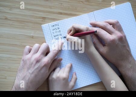 Vue de dessus du père adulte caucasien aidant sa fille ou son fils à faire les devoirs de maths sur l'arrière-plan de bureau en bois de cahier Banque D'Images